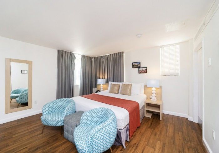 Bright bedroom with white walls, wood floor, bed, bedside table, mirror, and blue ottomans