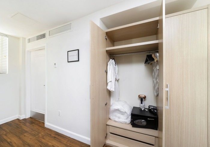 Open closet with shelves, hanging clothes, drawers, and a vacuum in a bright bedroom with hardwood floors