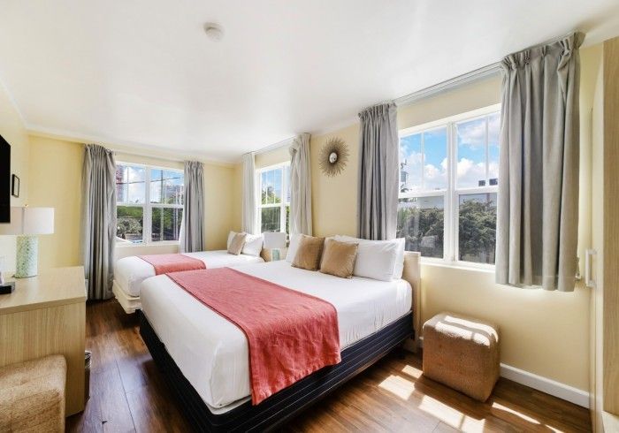 Bright bedroom with king bed, coral throw, and large windows with gray curtains