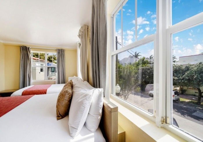 Bright bedroom with twin beds and large windows overlooking a sunny street and greenery