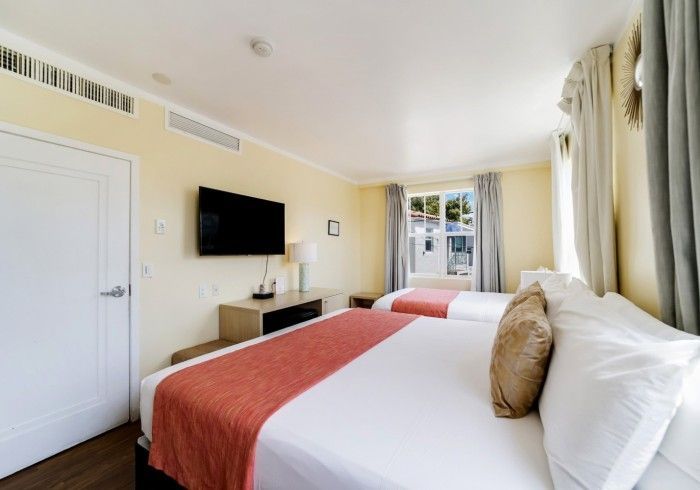 Bright hotel room with two beds, wall-mounted TV, and window curtains