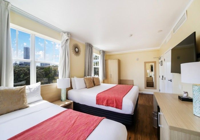 Bright hotel room with two twin beds, large windows, TV, and beige decor
