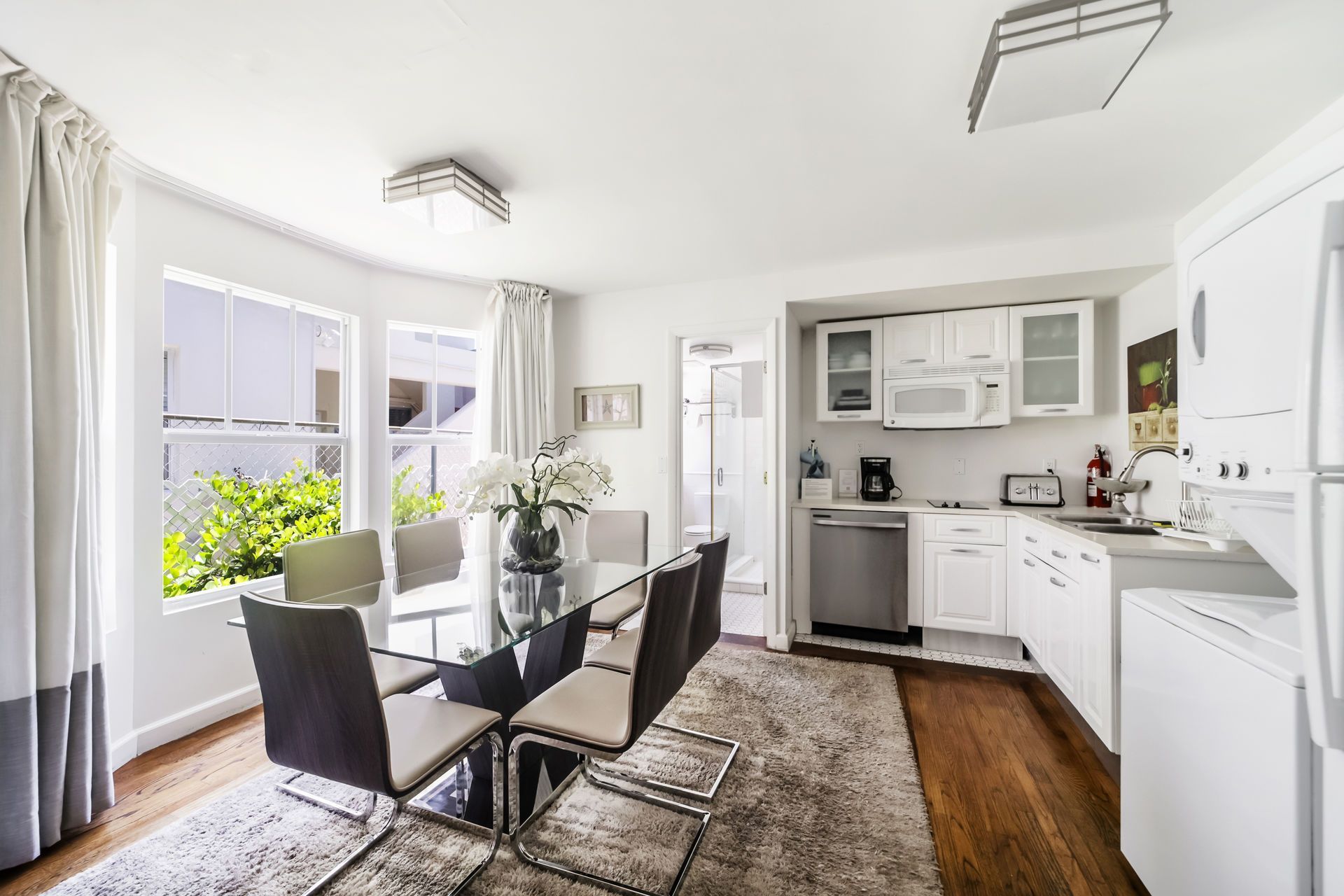 Bright dining area with glass table, white cabinetry, hardwood floor, and large windows overlooking greenery