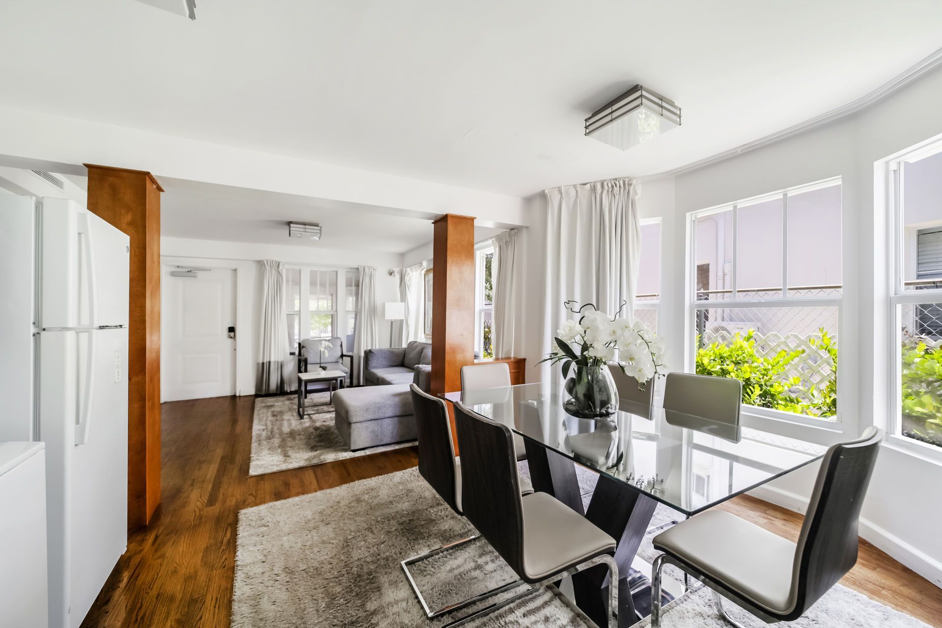 Bright dining room with glass table, black chairs, white walls, and large windows with city view