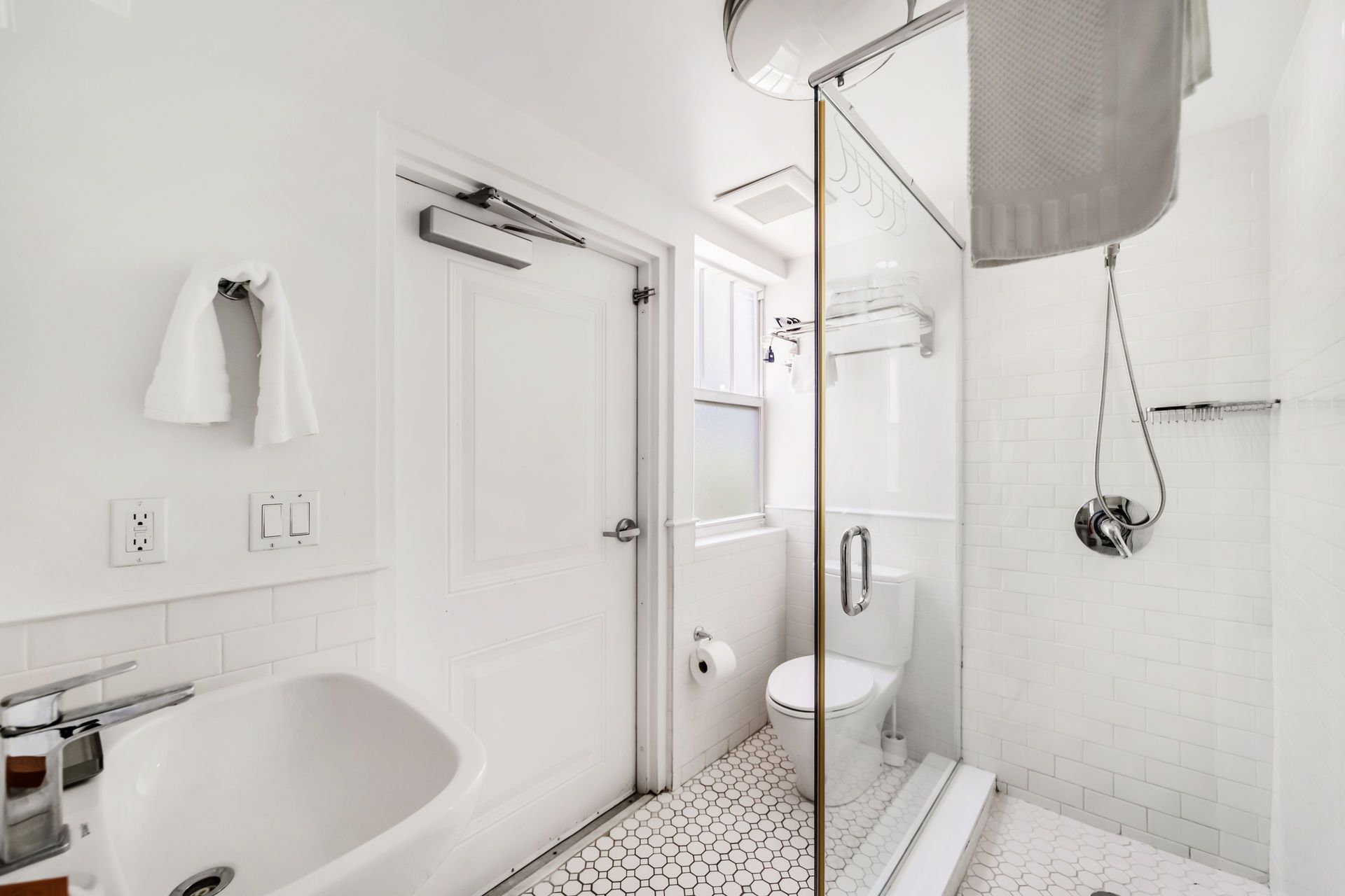 Bright white bathroom with sink, toilet, glass shower, and black-and-white tile floor