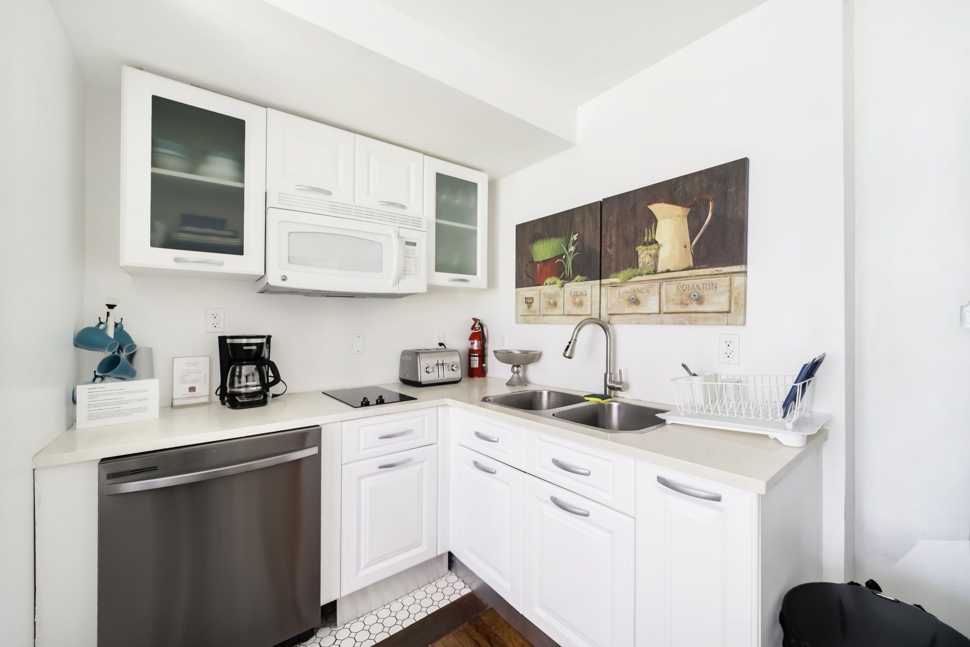 Bright white kitchen with cabinets, microwave, dishwasher, coffee maker, and wall art.