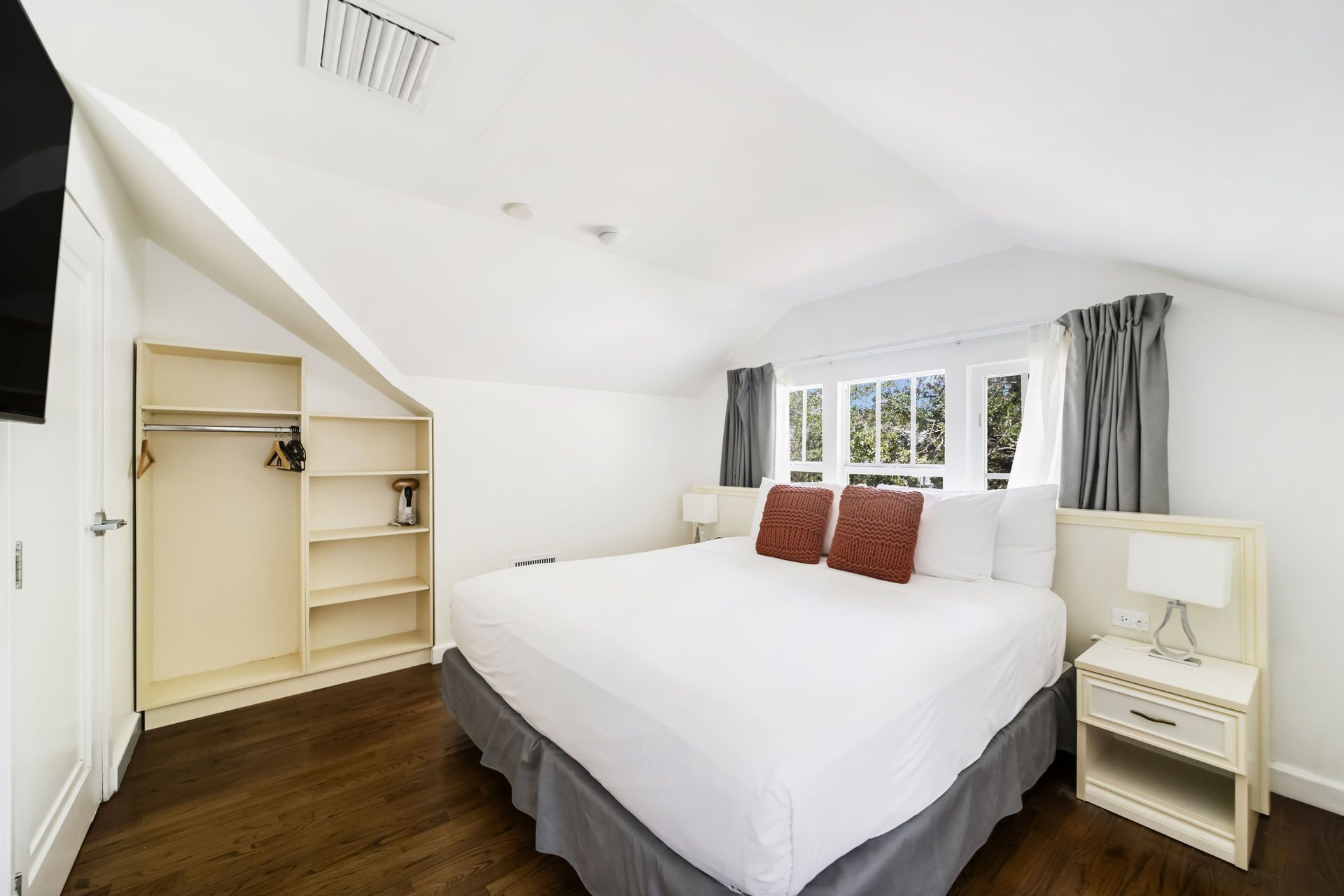 Bright bedroom with a white bed, gray curtains, wood floor, and open closet shelves