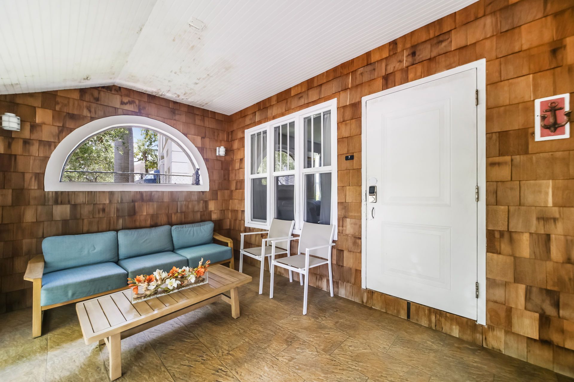Cozy sunroom with blue sofa, coffee table, white chairs, and wood-paneled walls.