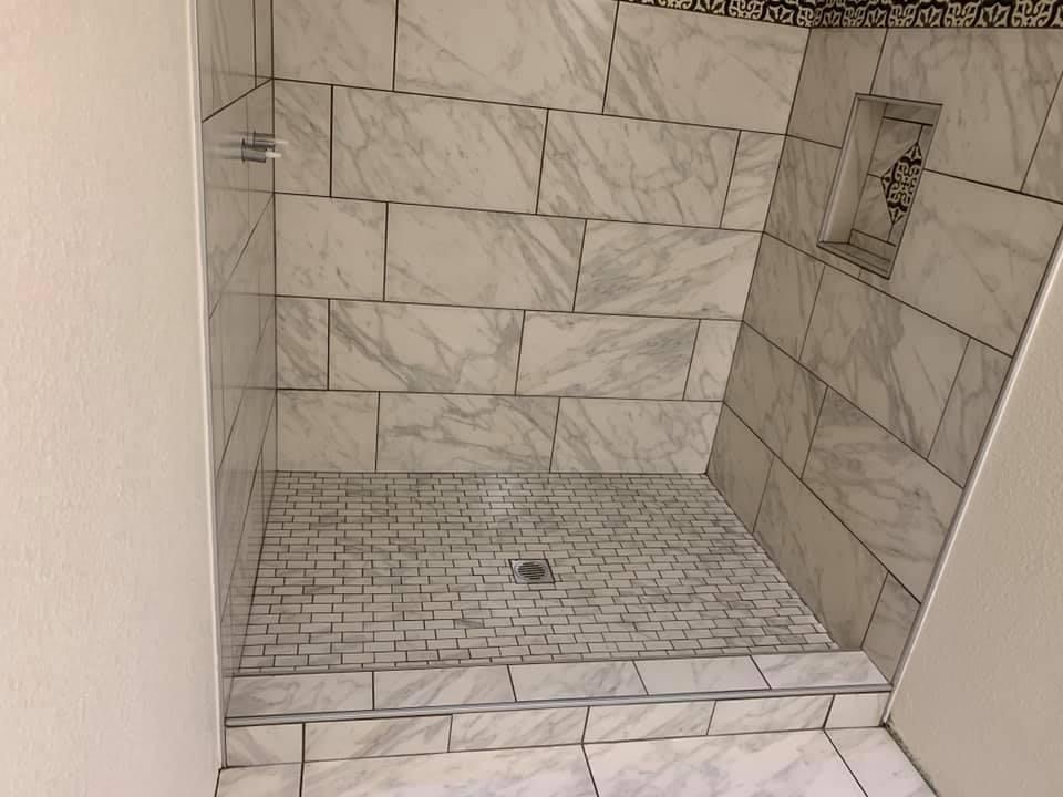 A shower stall with white tiles and a drain in a bathroom by remodeling contractors.
