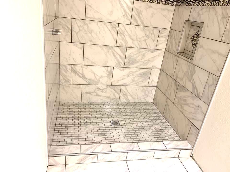 A shower stall with white tiles and a drain in a bathroom by remodeling company.