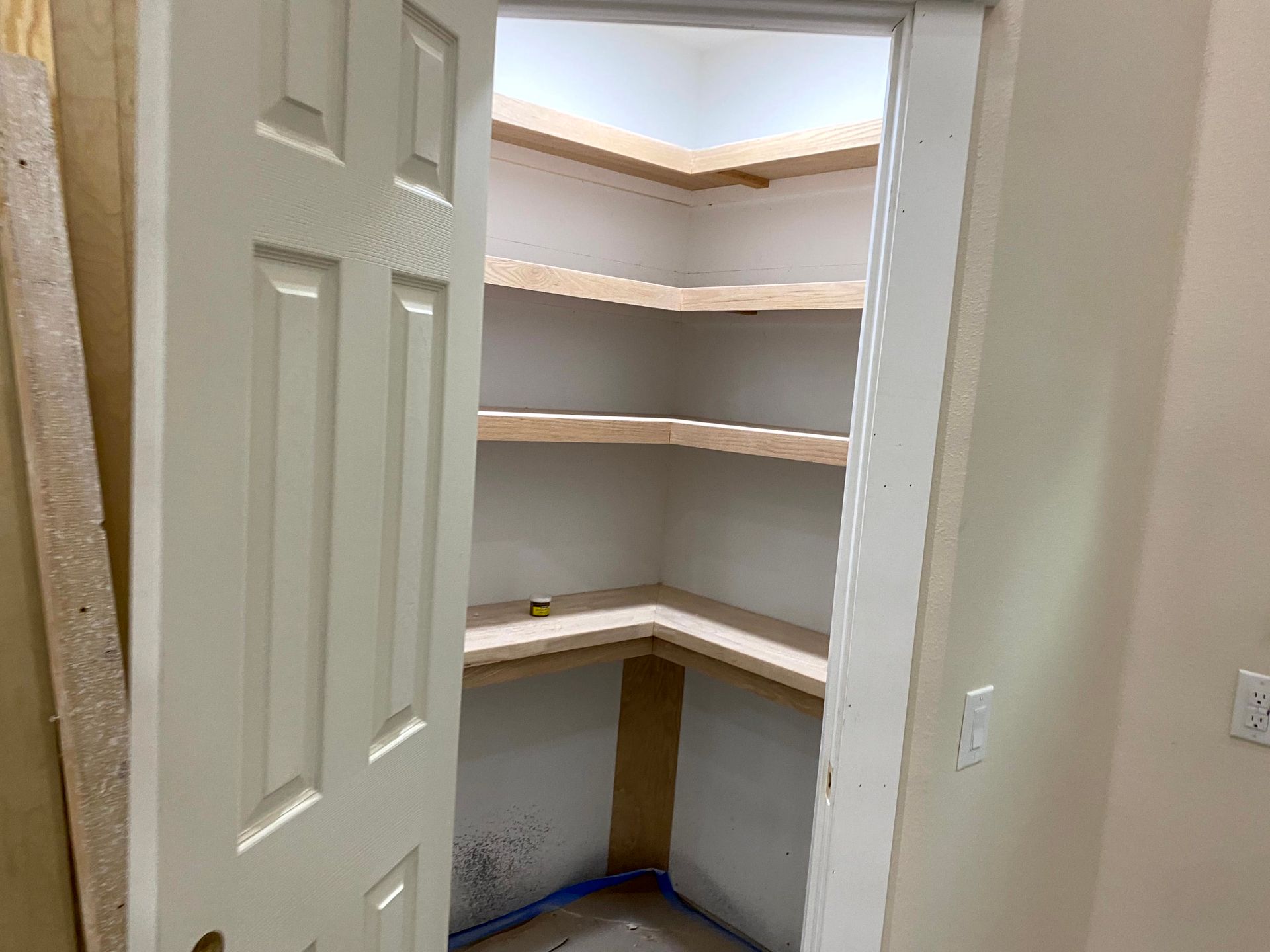 A pantry with shelves and a door is being built in a house by home renovating contractors.