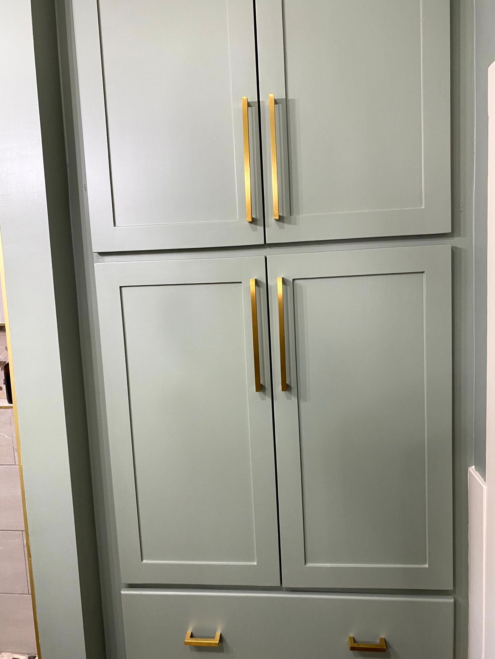 A white cabinet with gold handles and drawers in a room. Work complete by cabinet installer