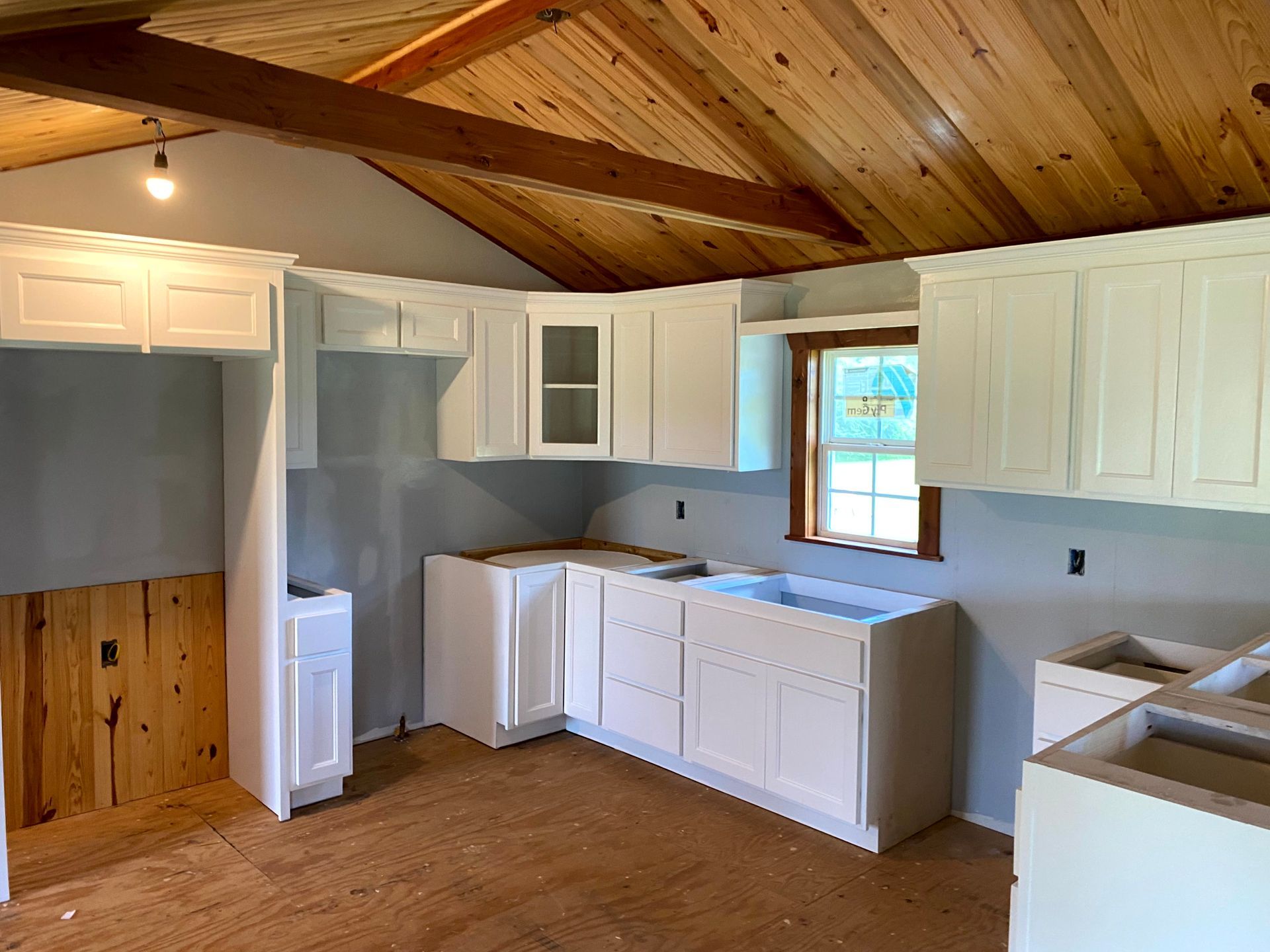 A kitchen with white cabinets and a wooden ceiling by remodeling contractors.