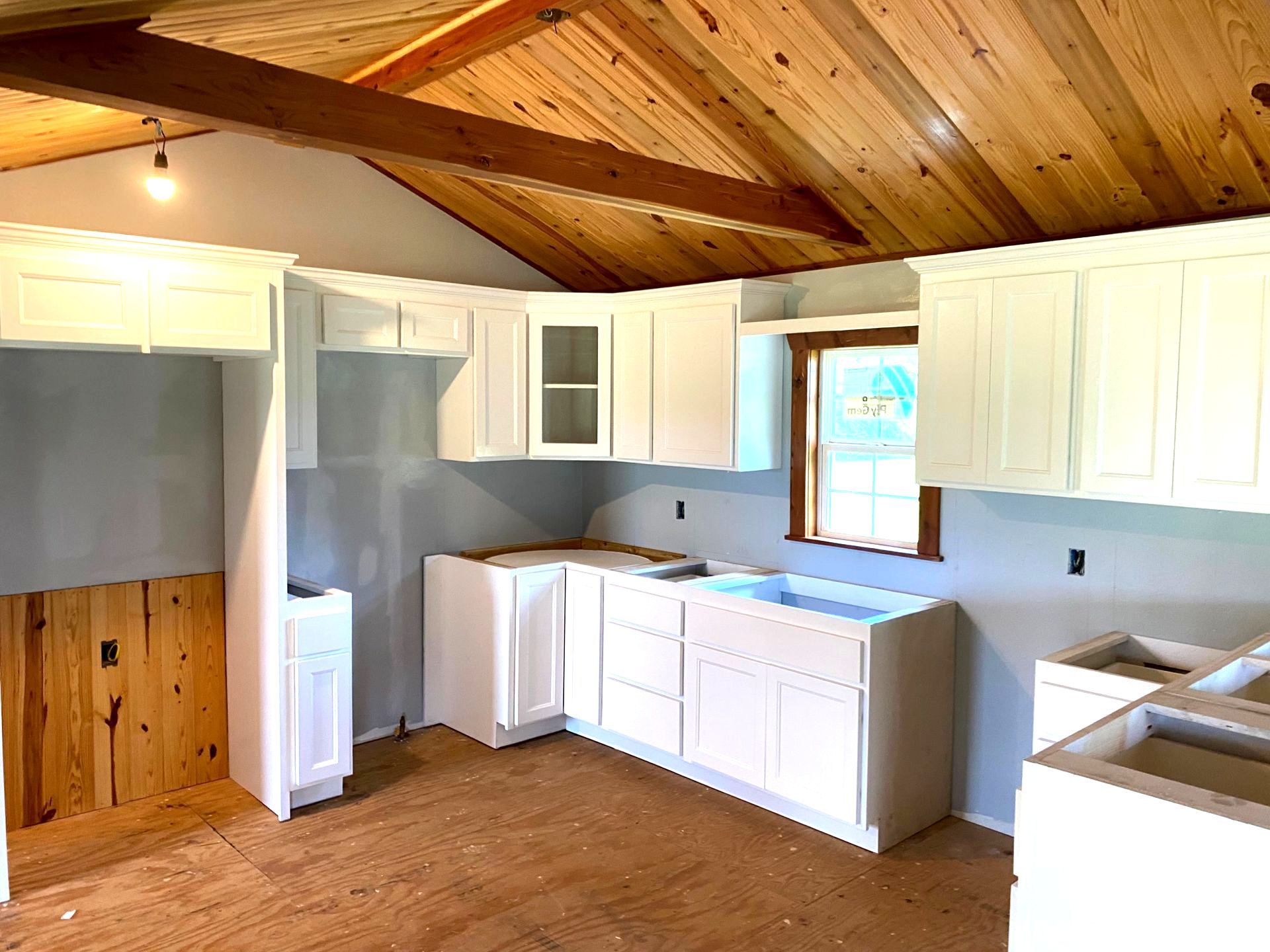 A kitchen with white cabinets and a wooden ceiling getting renovated.