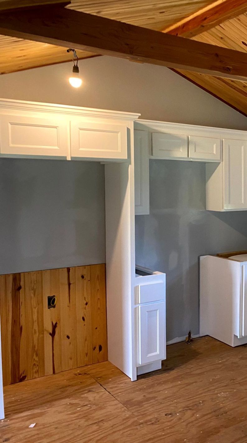 A kitchen under construction with white cabinets and wooden floors by remodeling contractors.