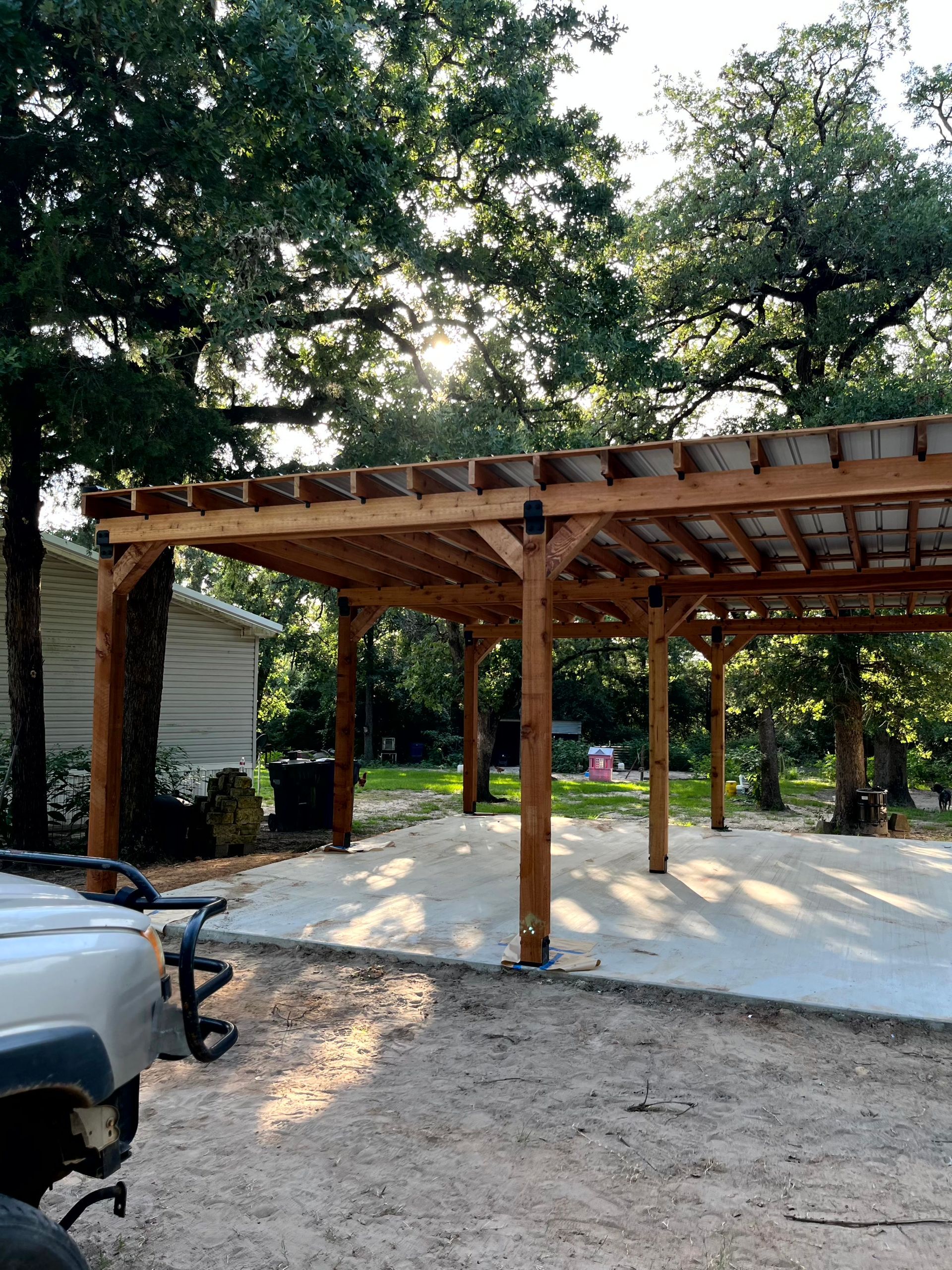 A car is parked under a wooden pergola in a driveway made by by remodeling contractors.