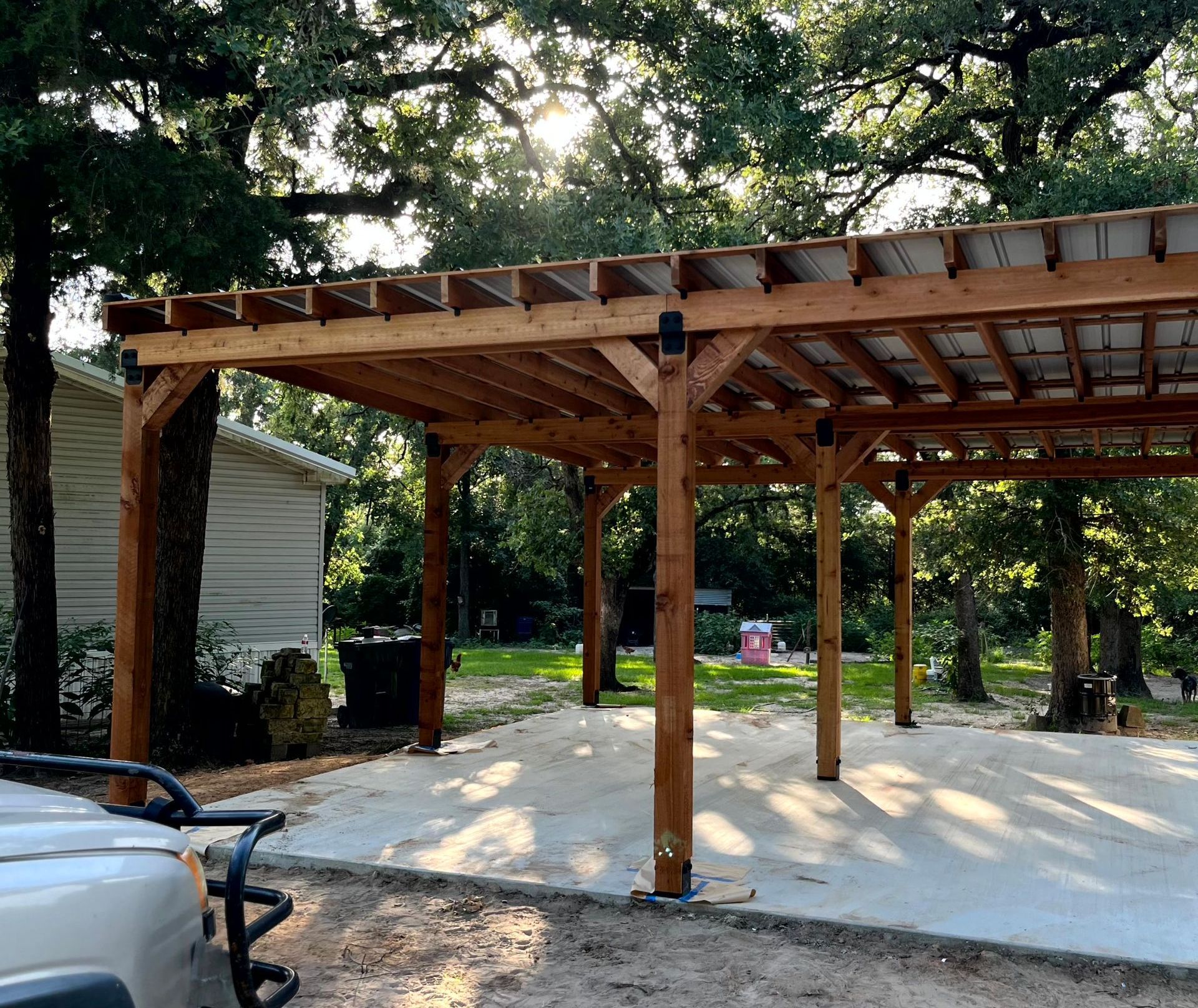 A white golf cart is parked under a wooden pergola by remodeling contractors.