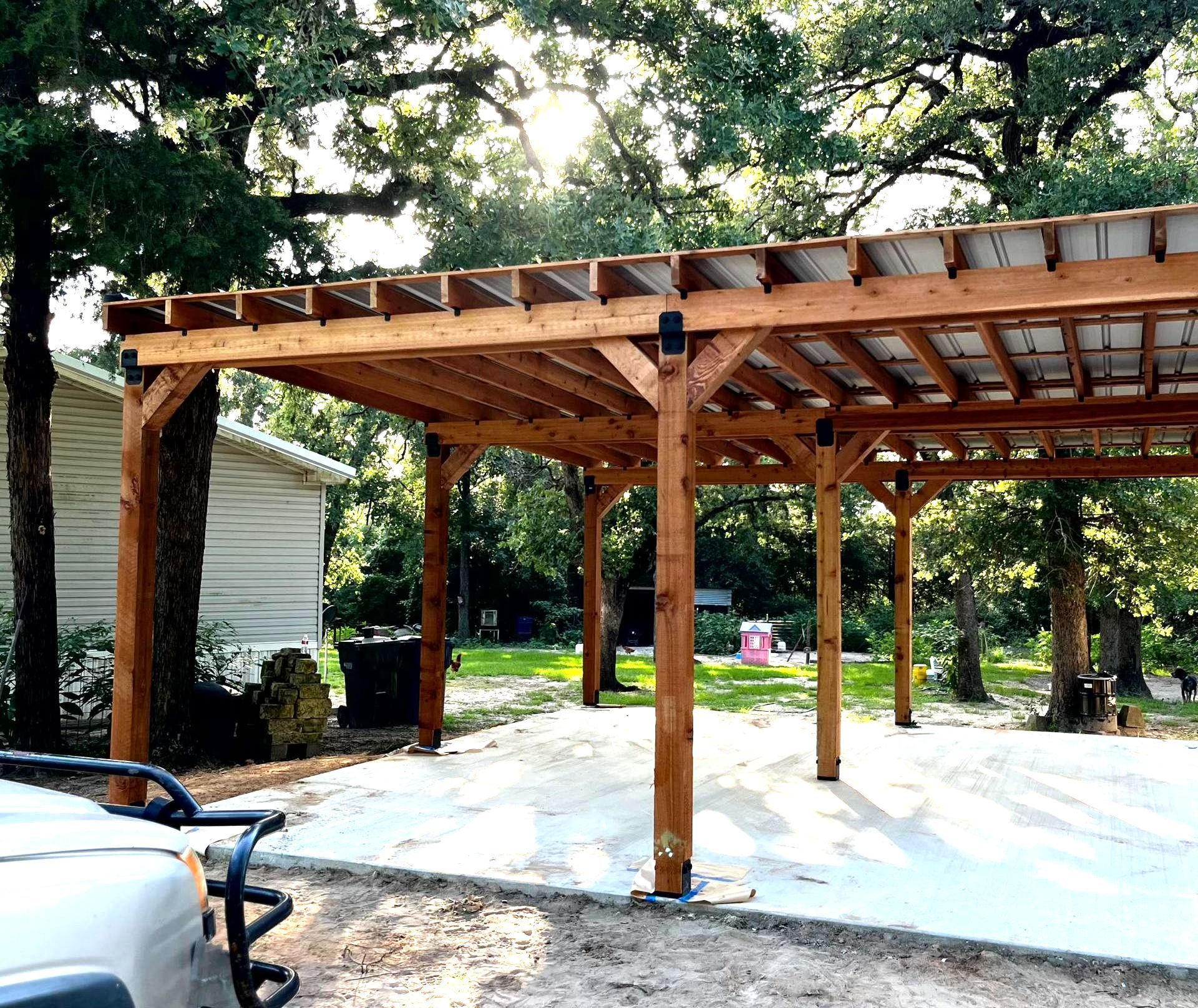 A car is parked under a wooden pergola in front of a house.