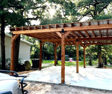 A car is parked under a wooden pergola in front of a house by home renovating contractors.