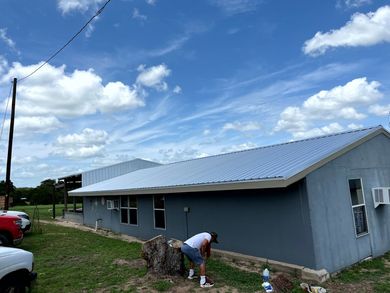 A remodeling contractors is painting the side of a house on a sunny day.