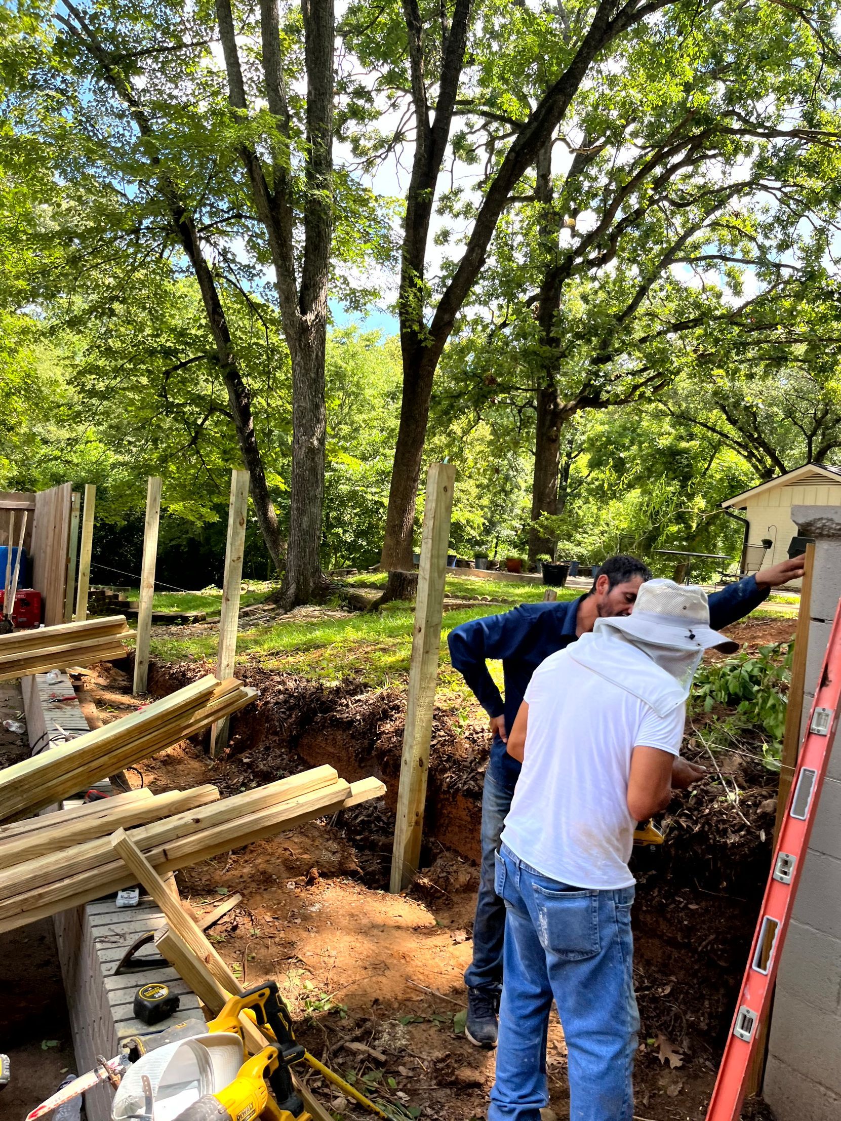 Two men are working on a fence in a backyard prepping the job.