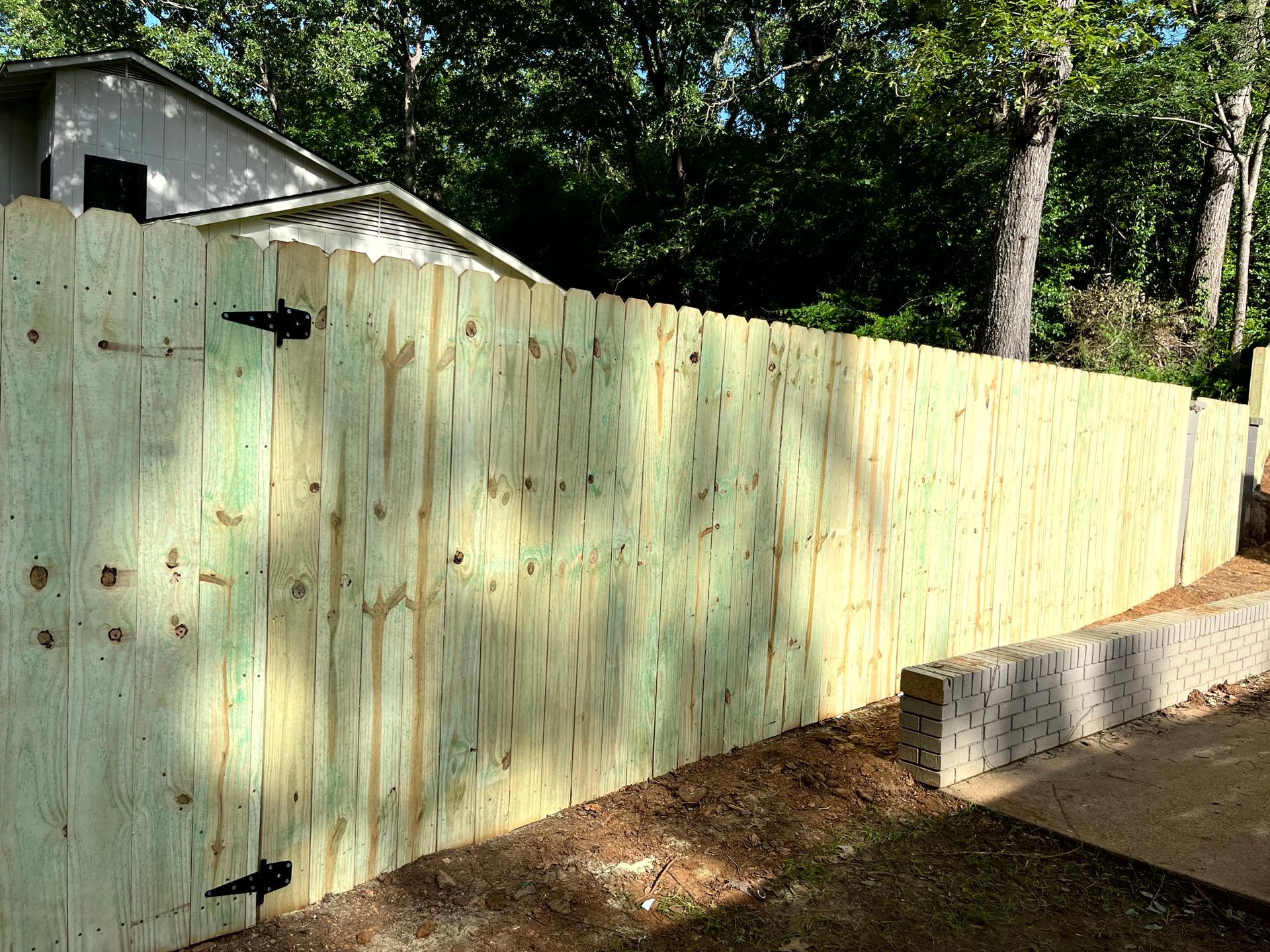 A wooden fence with a black gate is in front of a house by remodeling contractors.