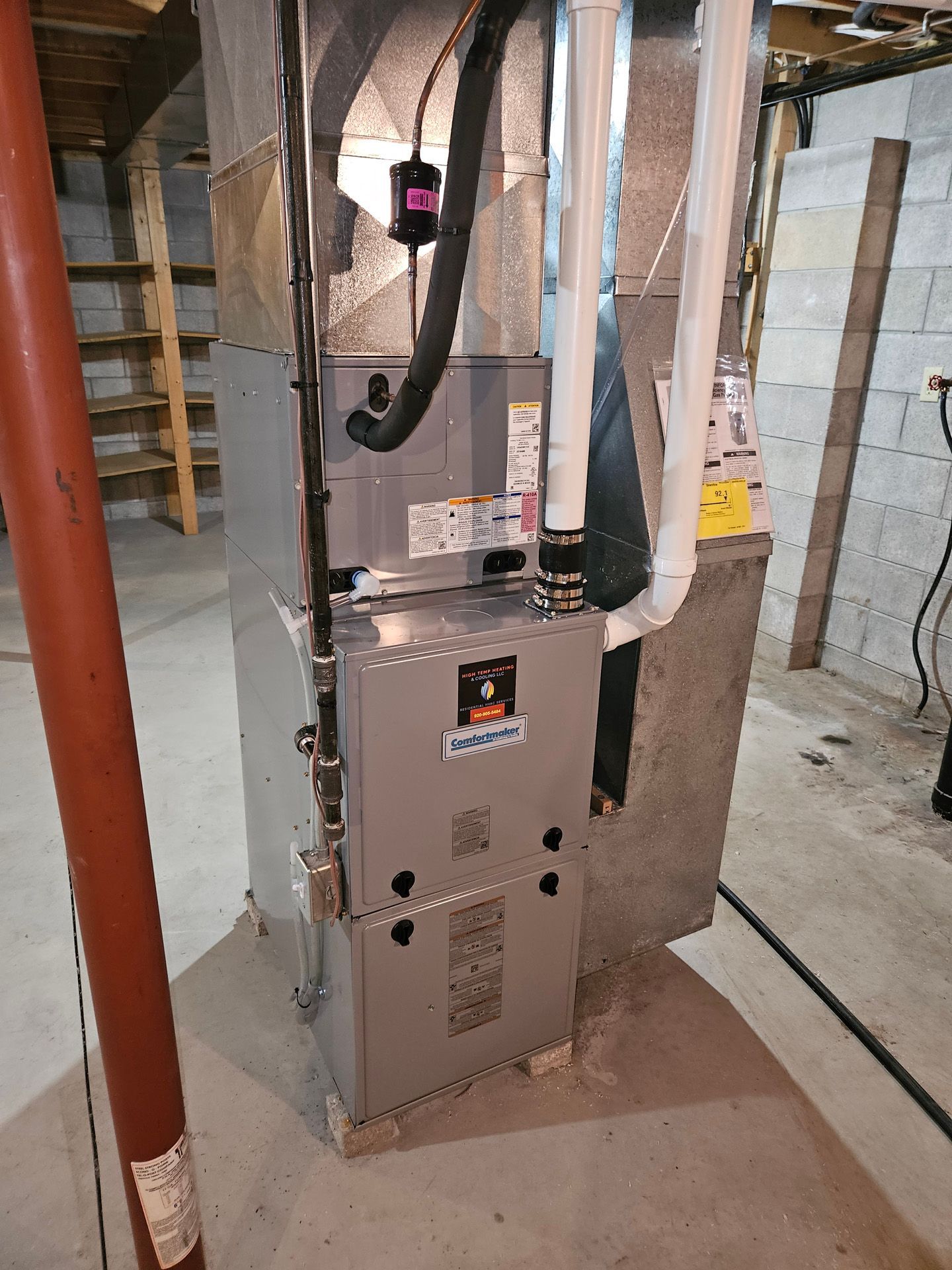 A furnace is sitting in a basement next to a pipe.