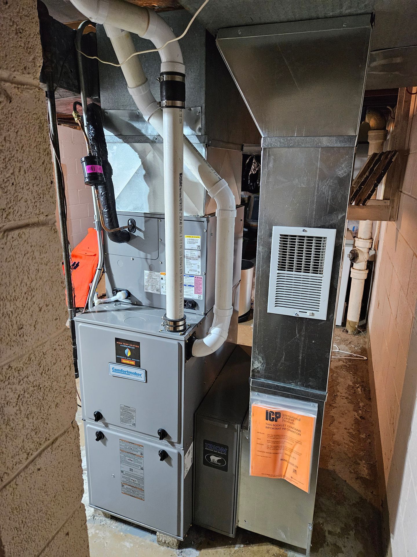 A furnace is sitting in a basement next to a wall.