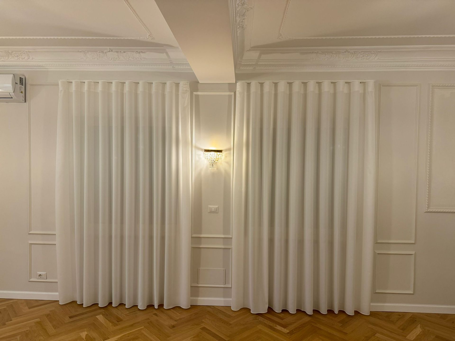 Un soggiorno con tende bianche e pavimento in legno.