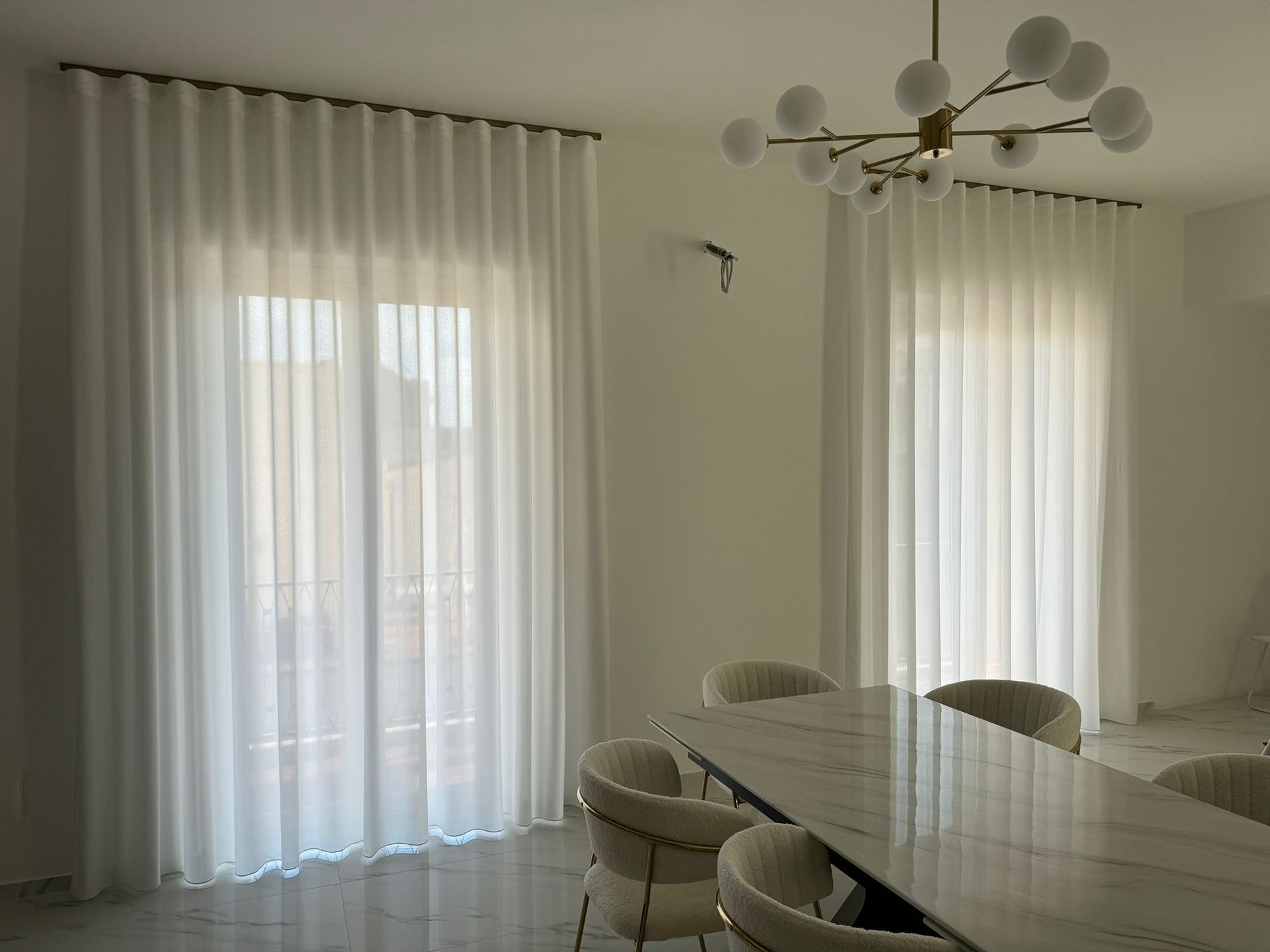 Una sala da pranzo con tavolo, sedie e tende bianche.