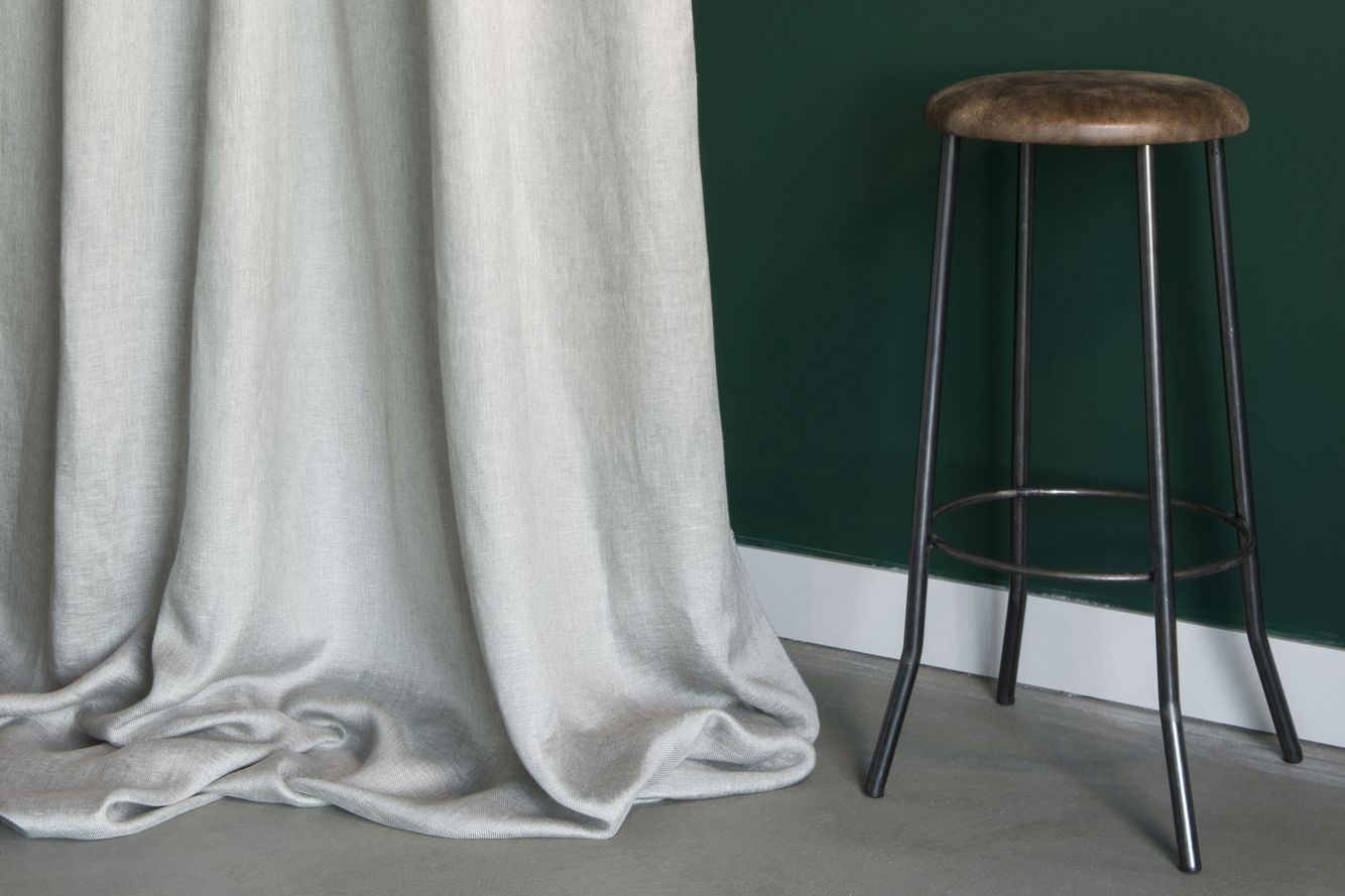 Uno sgabello da bar è appoggiato accanto a una tenda bianca in una stanza.