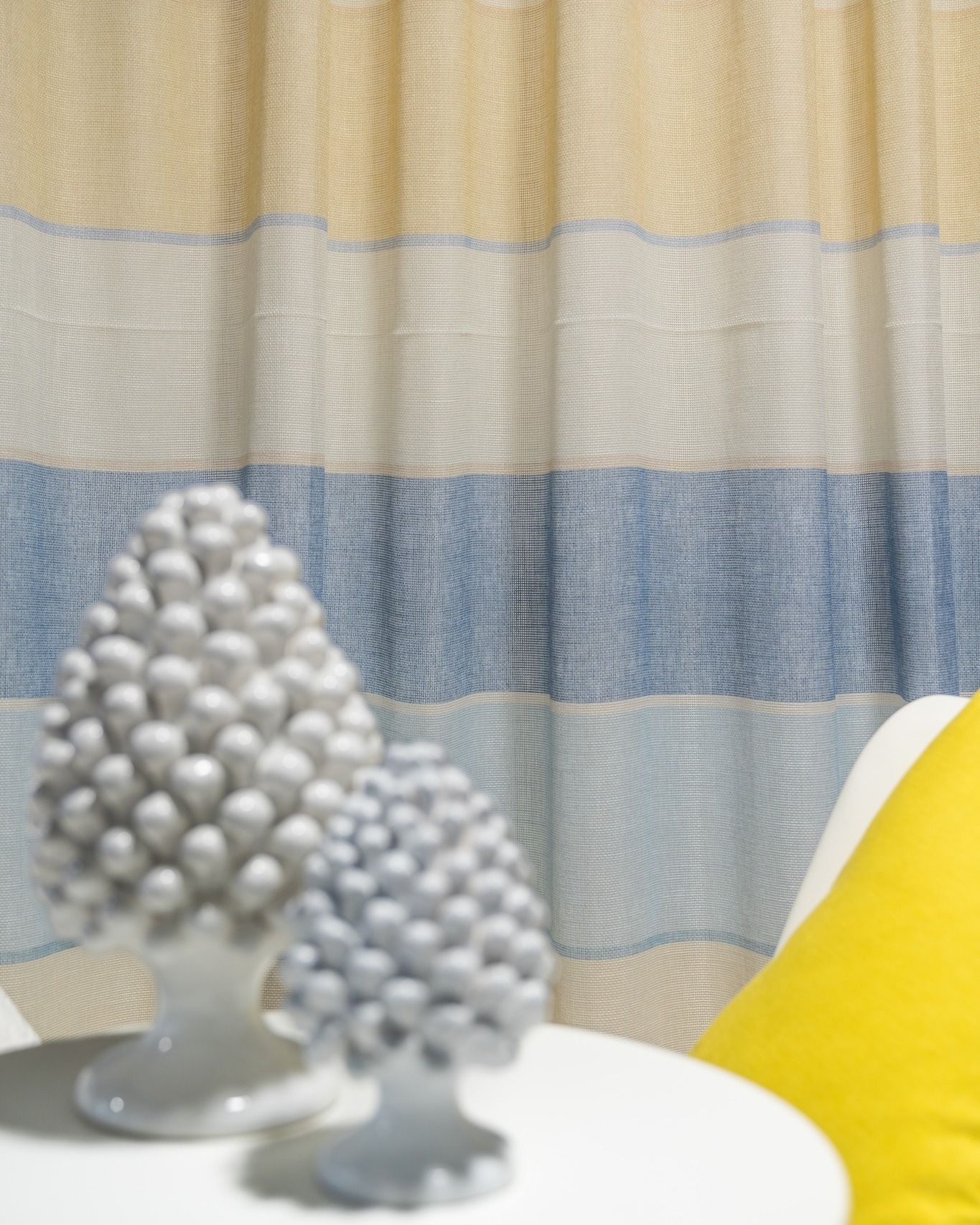 Un cuscino giallo è appoggiato su un tavolo bianco davanti a una tenda a strisce