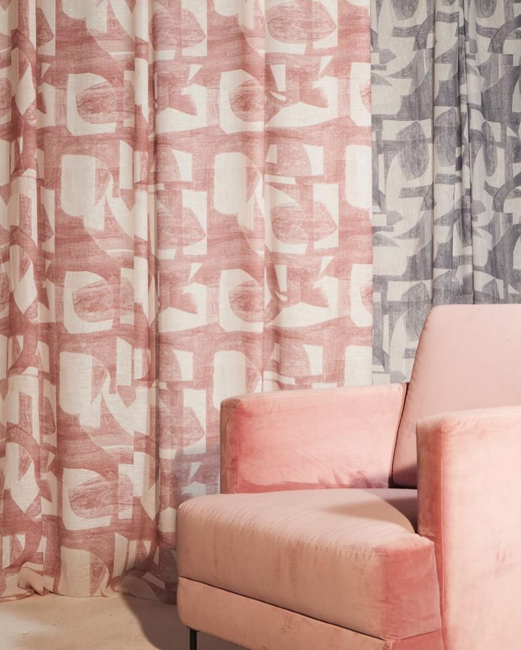 Una sedia rosa è seduta davanti a un paio di tende rosa