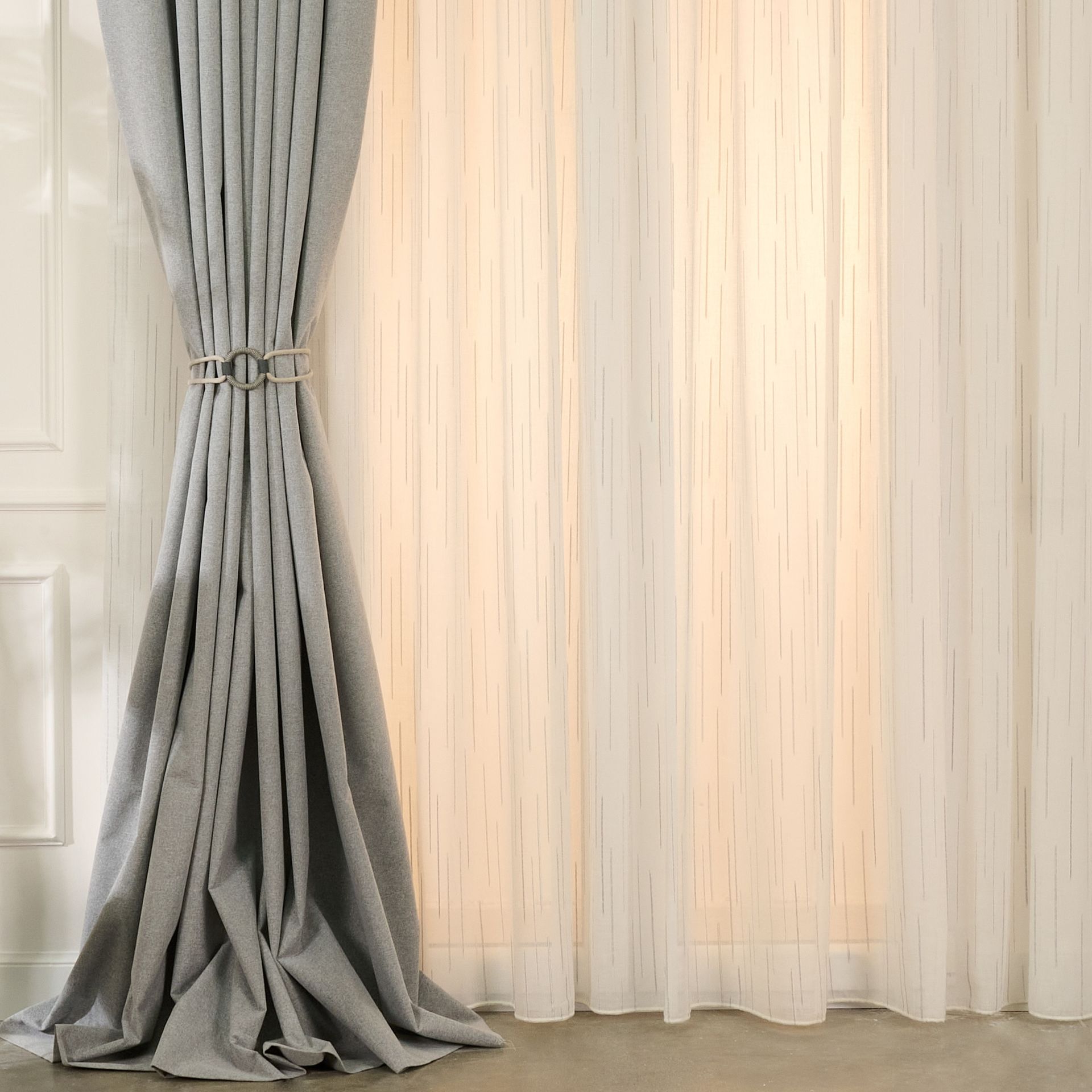 Un paio di tende grigie appese a una finestra accanto a una tenda bianca.