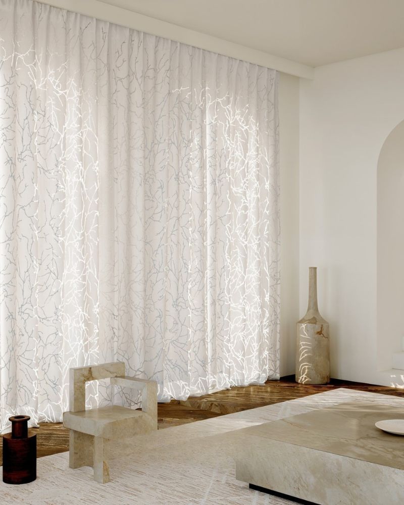 Un soggiorno con tende bianche, una sedia, un tavolo e vasi.