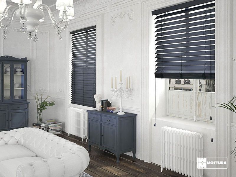 Un soggiorno con divano, cassettiera e due finestre con persiane.