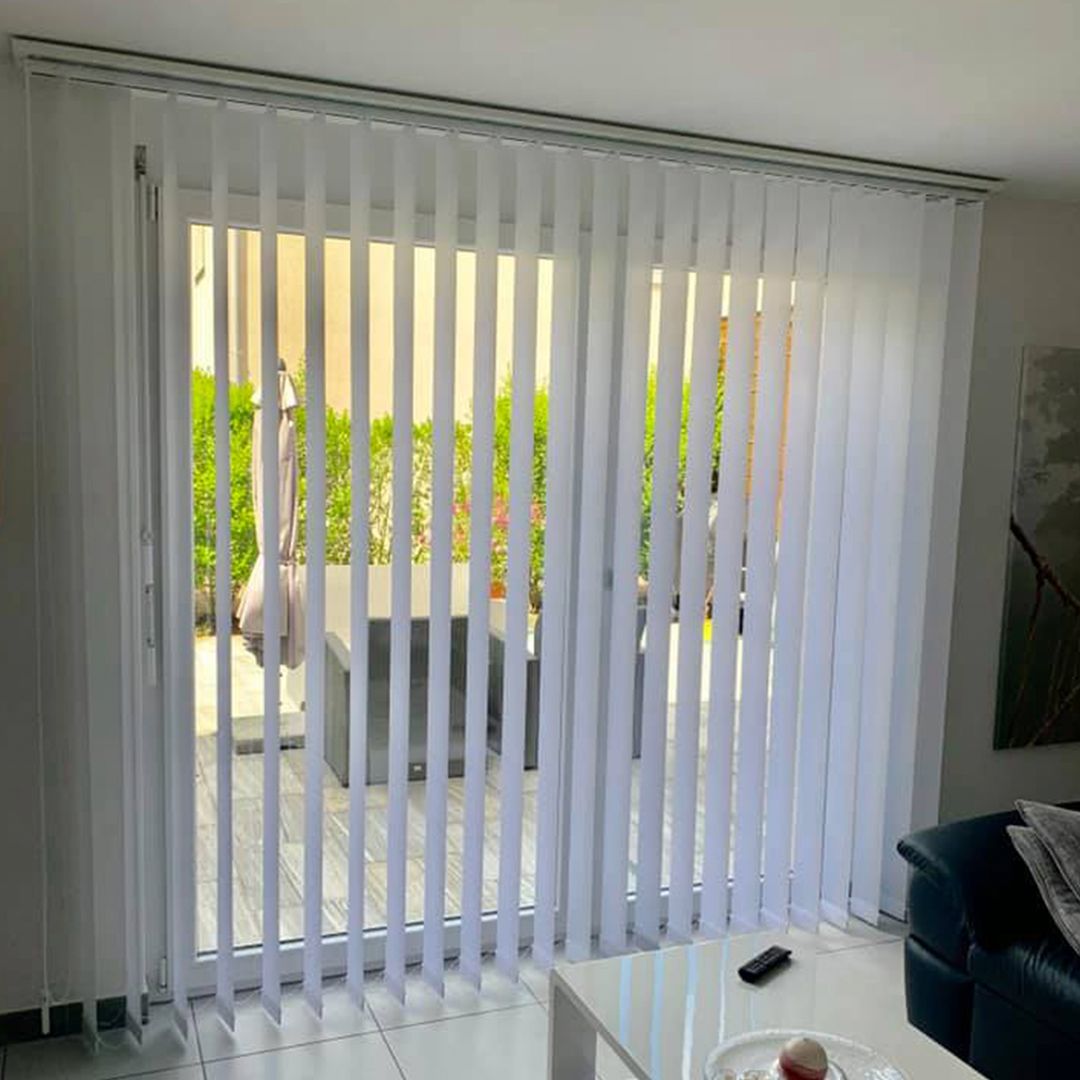 Un soggiorno con una porta scorrevole in vetro e persiane verticali bianche.