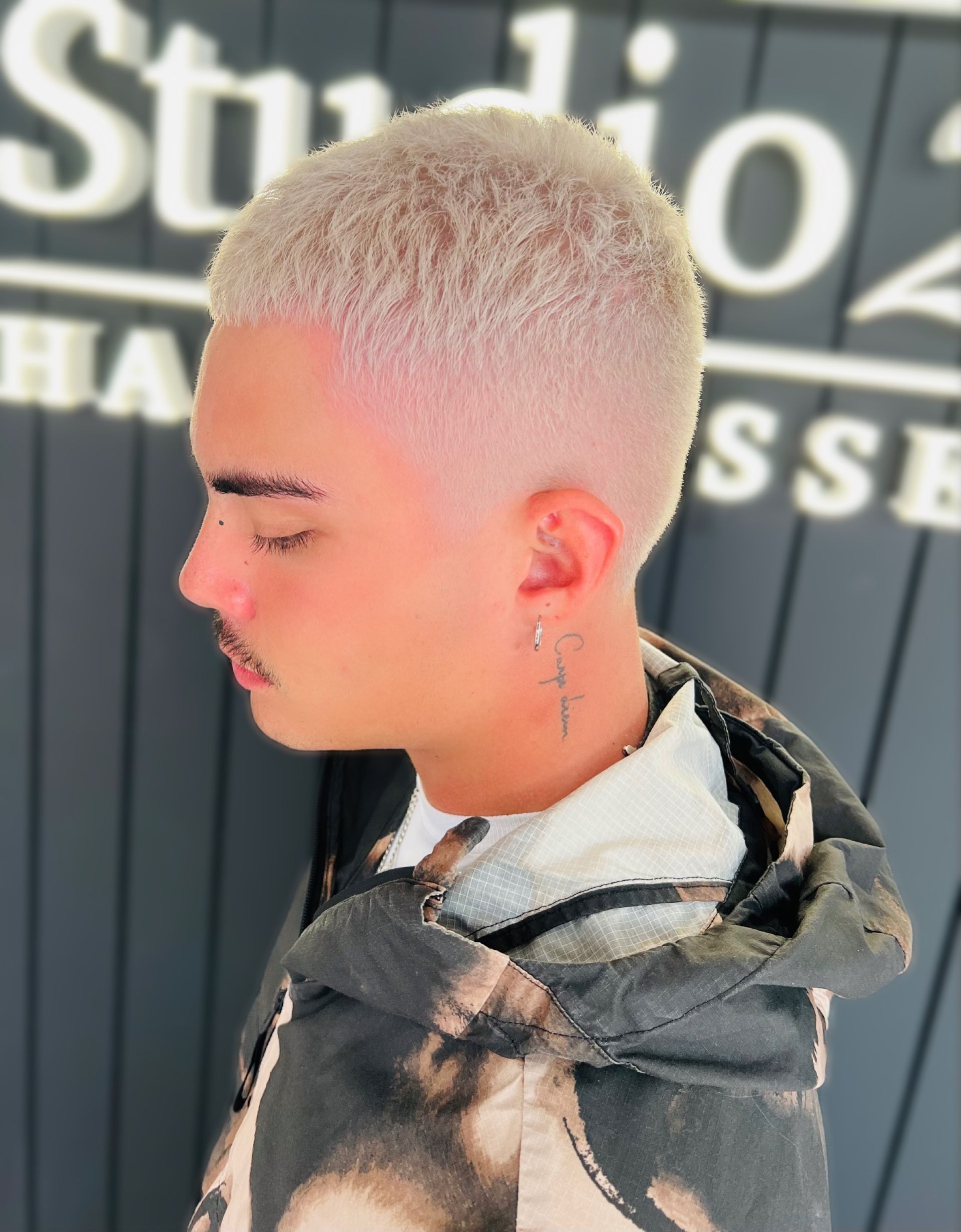 Man with bleached blonde hair and faded sides, wearing a hoodie, posing near a salon sign — Studio 23 In Biggera Waters, QLD