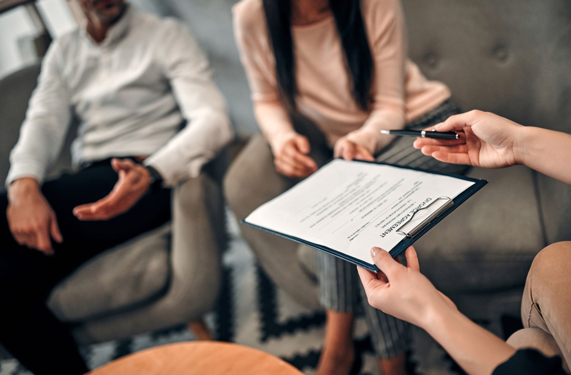 Meeting notes being reviewed on a clipboard while two people sit on a couch in the background