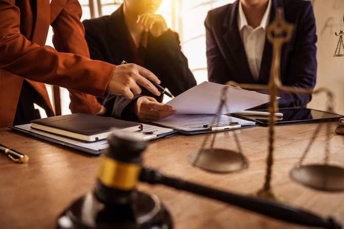 Lawyers reviewing documents at a desk beside a balance scale and gavel in a courtroom setting