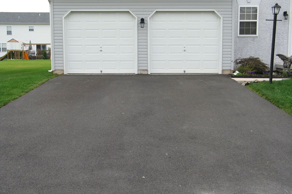 A Driveway Leading to a Garage With Two White Garage Doors | Round Lake, IL | Korinek & Son Concrete and Asphalt