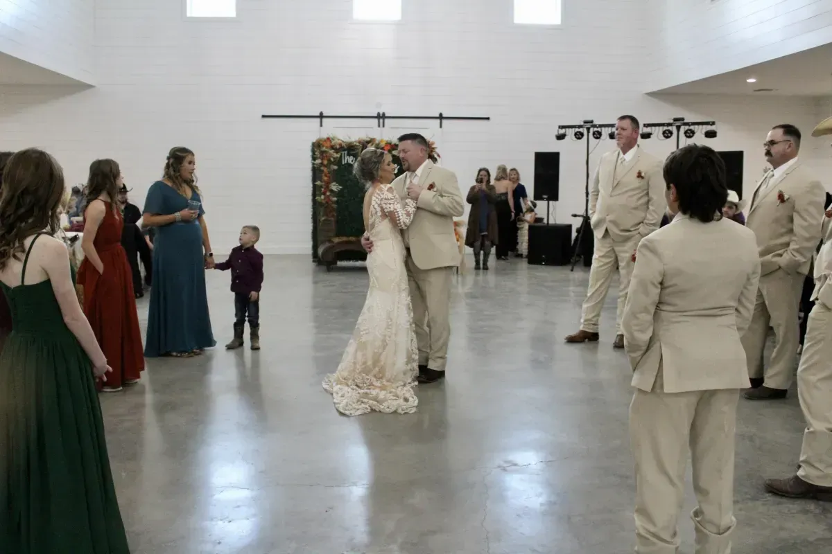 A bride and groom are dancing at their wedding reception while their wedding party watches.