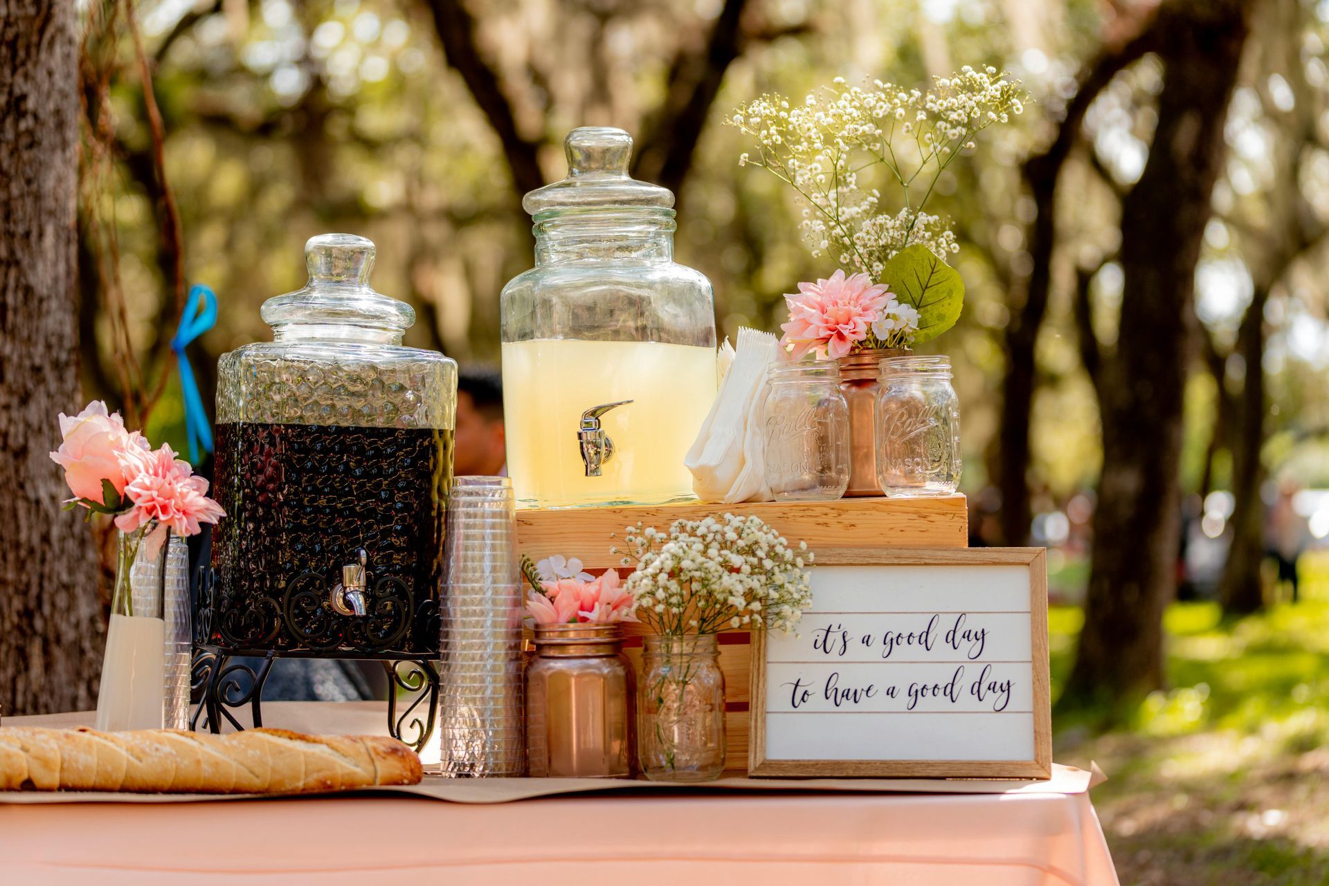 A table with bottles of lemonade , flowers , and a sign on it.