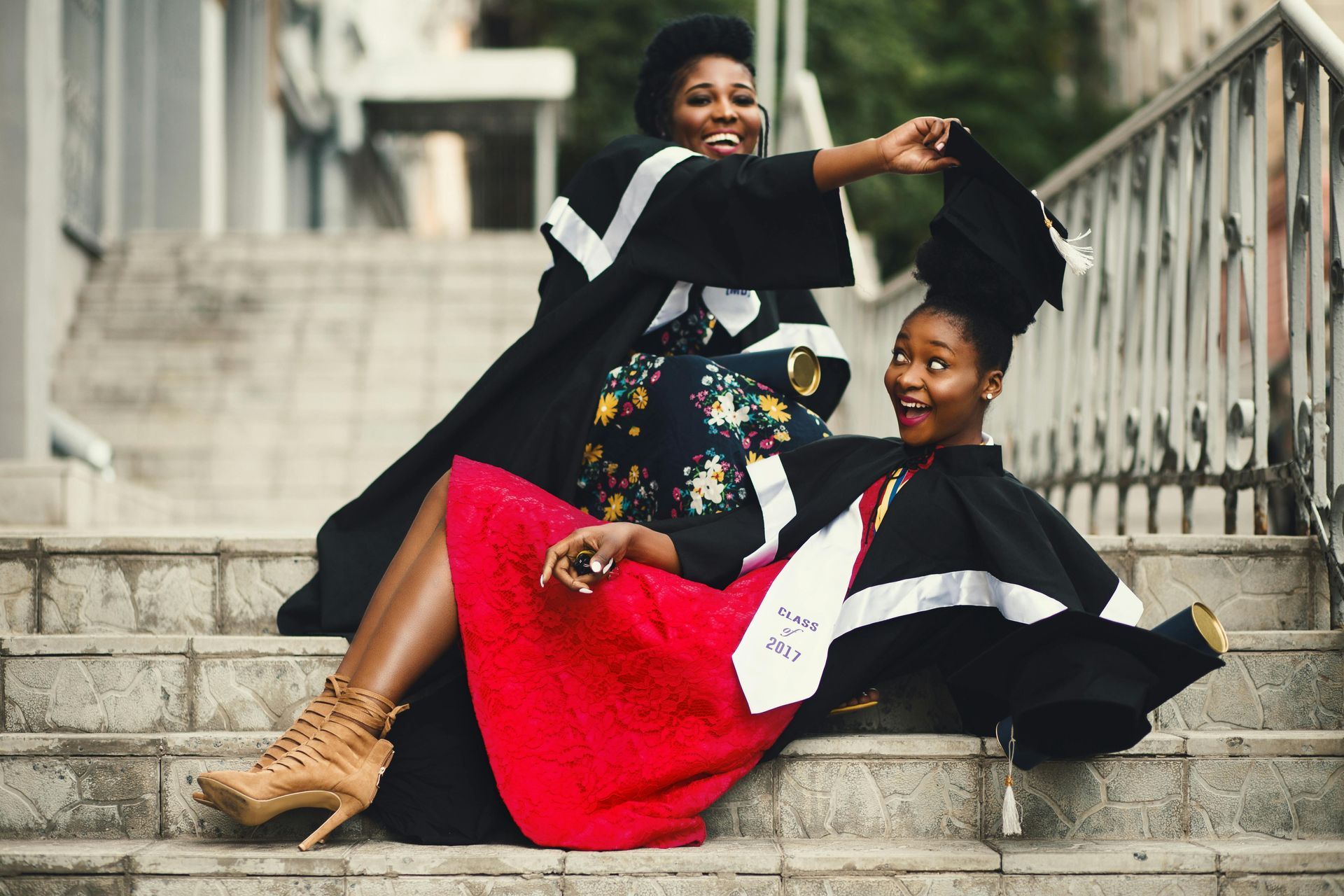 Two women in graduation gowns are sitting on a set of stairs.