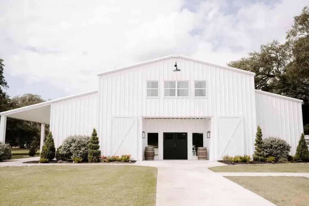 A large white barn with a black door and a walkway leading to it.