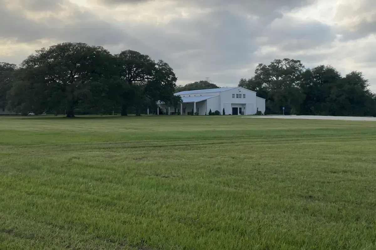 A large white house is sitting in the middle of a lush green field.