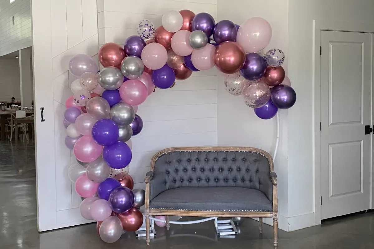 A couch is sitting under a balloon arch in a room.