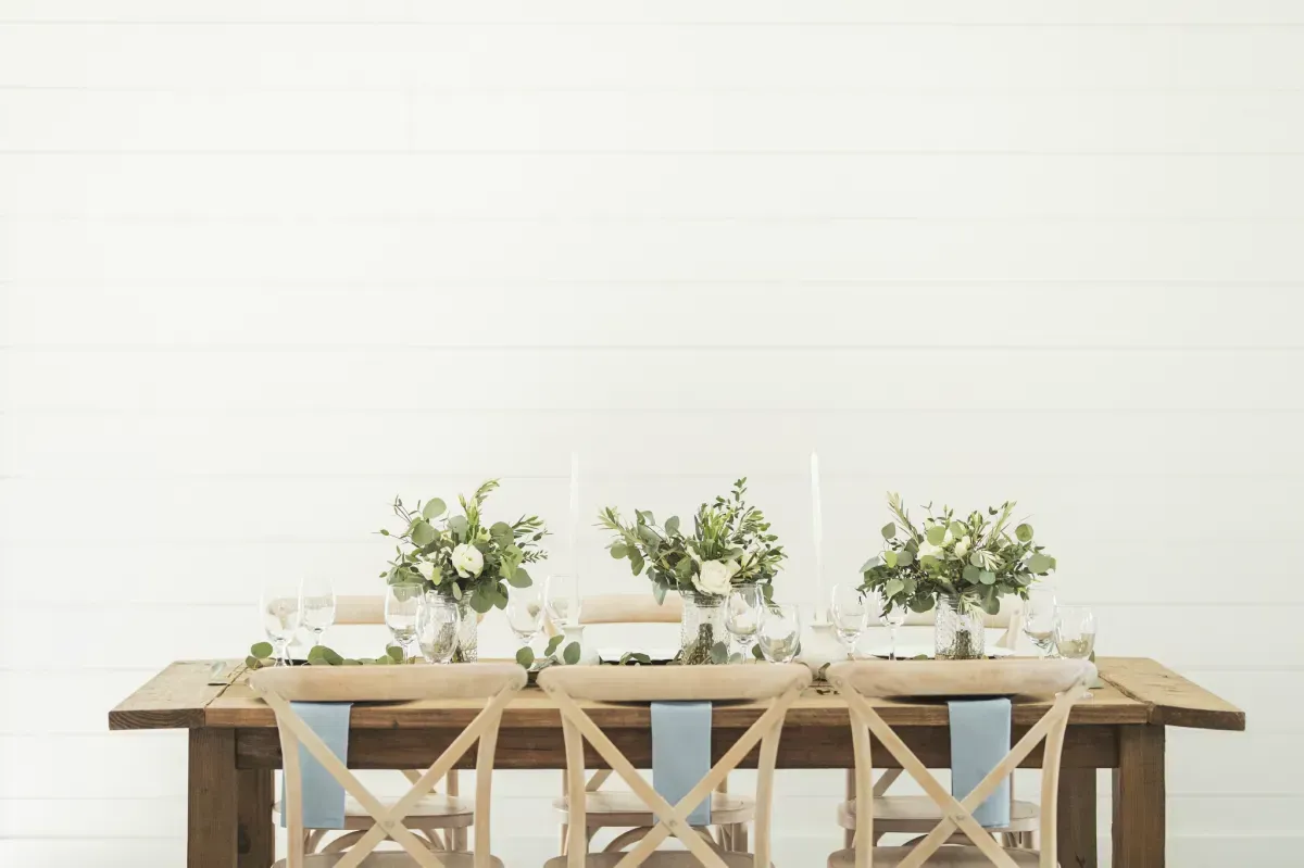 A long wooden table with chairs and flowers on it.