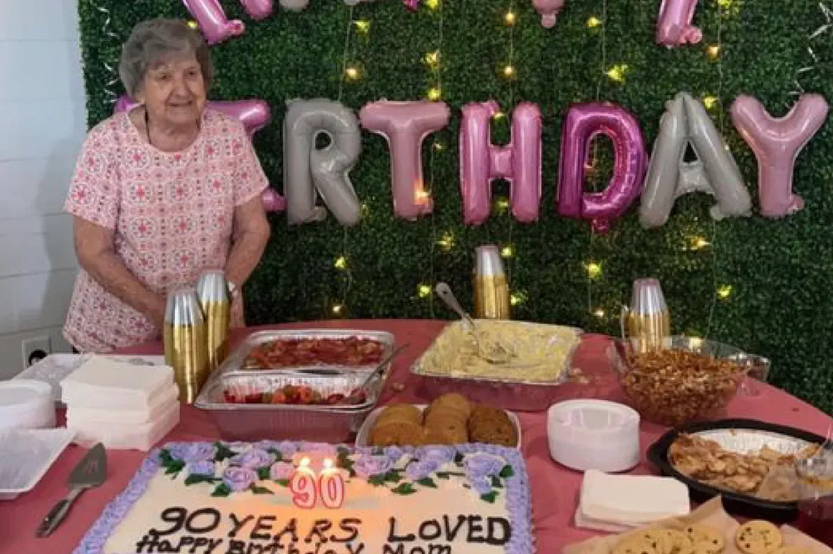 An elderly woman is standing in front of a birthday cake.
