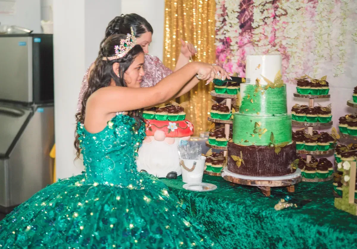 A woman in a green dress is cutting a cake.